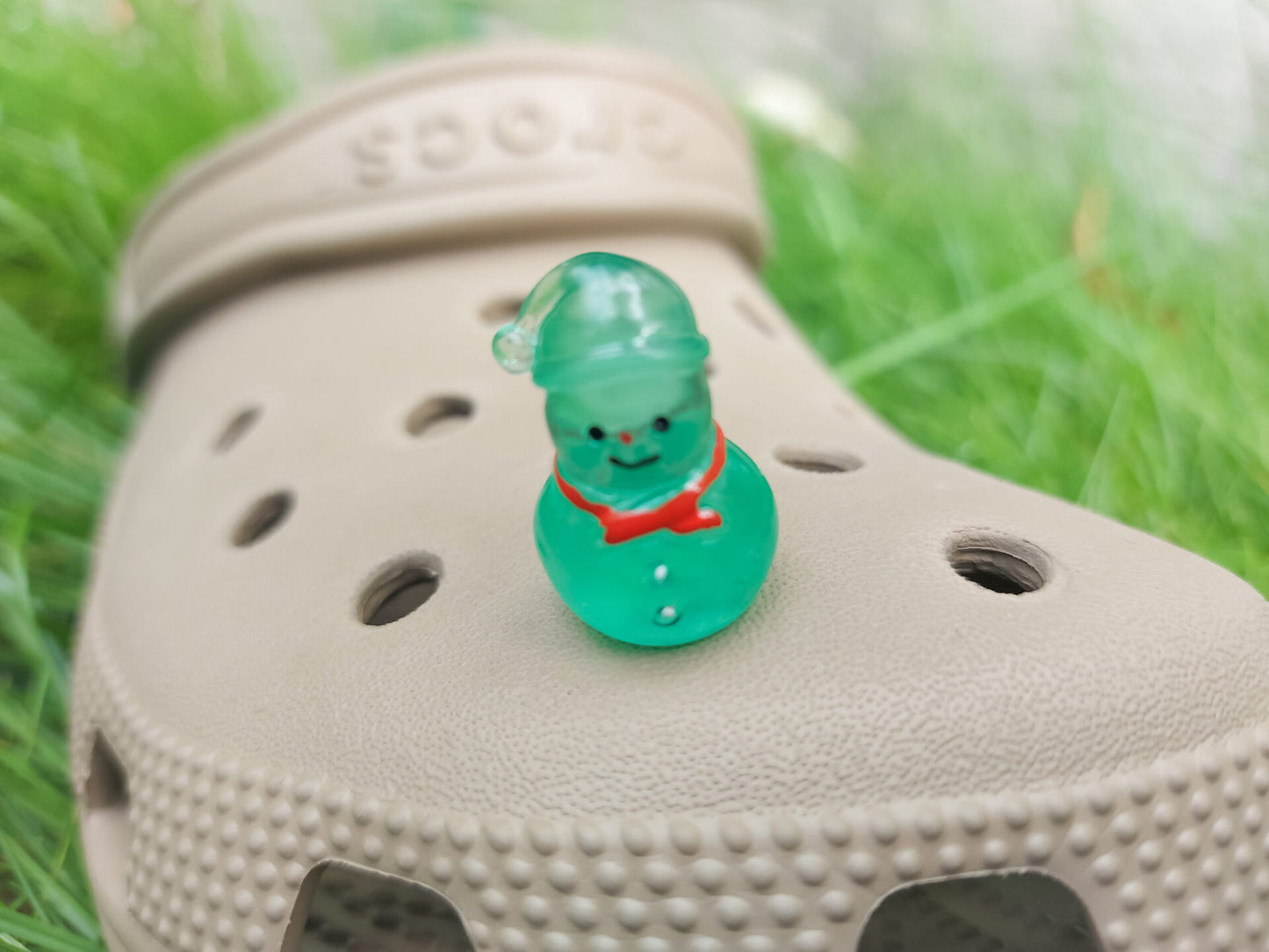 Glow-in-the-dark snowmen charms adorning a beige shoes shoe. The snowmen are in vibrant colors like green, yellow, red, purple, orange, and blue. Each snowman has a scarf, and a small hat, radiating a festive vibe perfect for the holiday season.