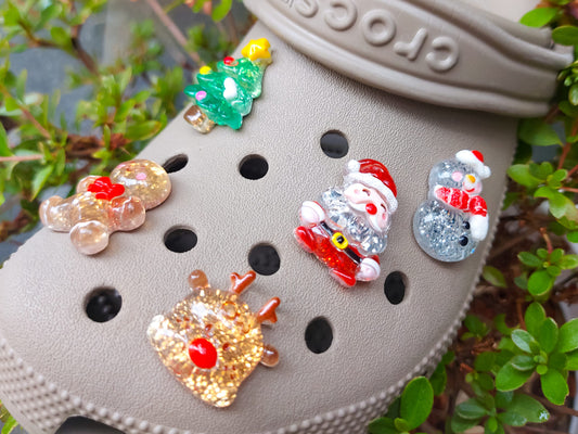 A glittery Christmas-themed set of five shoe charms featuring a gingerbread man, reindeer, snowman, Santa, and a Christmas tree. Each charm has a sparkling glitter finish, adding a festive and playful holiday touch to your shoes.