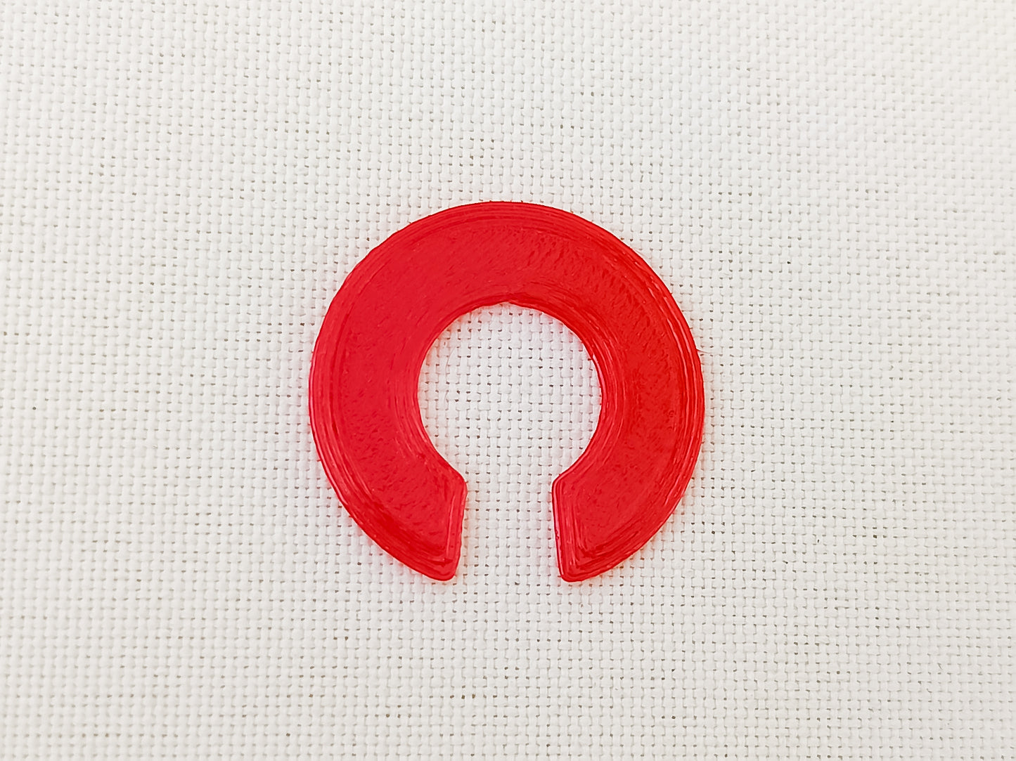 Close-up of a red 3D printed TPU shoe charm Clip designed to secure charms from falling out. The clip is flexible and fits onto the back of charms, fastening them securely to the inside of shoes shoes for added protection during wear.