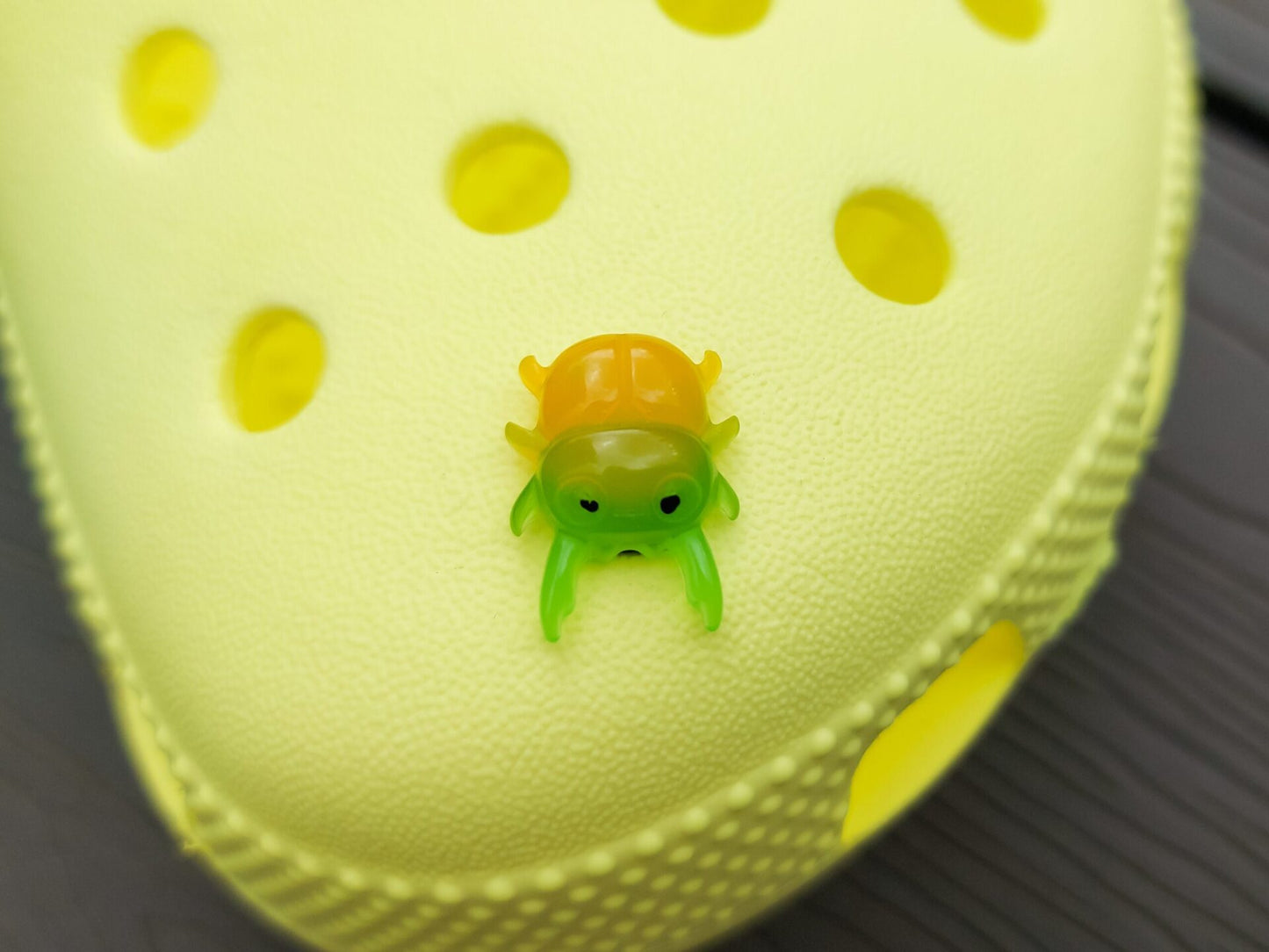 A vibrant collection of beetle-themed shoe charms decorates a yellow shoes shoe. The charms feature detailed, multicolored beetles in various shades, adding a playful yet nature-inspired vibe to the footwear.