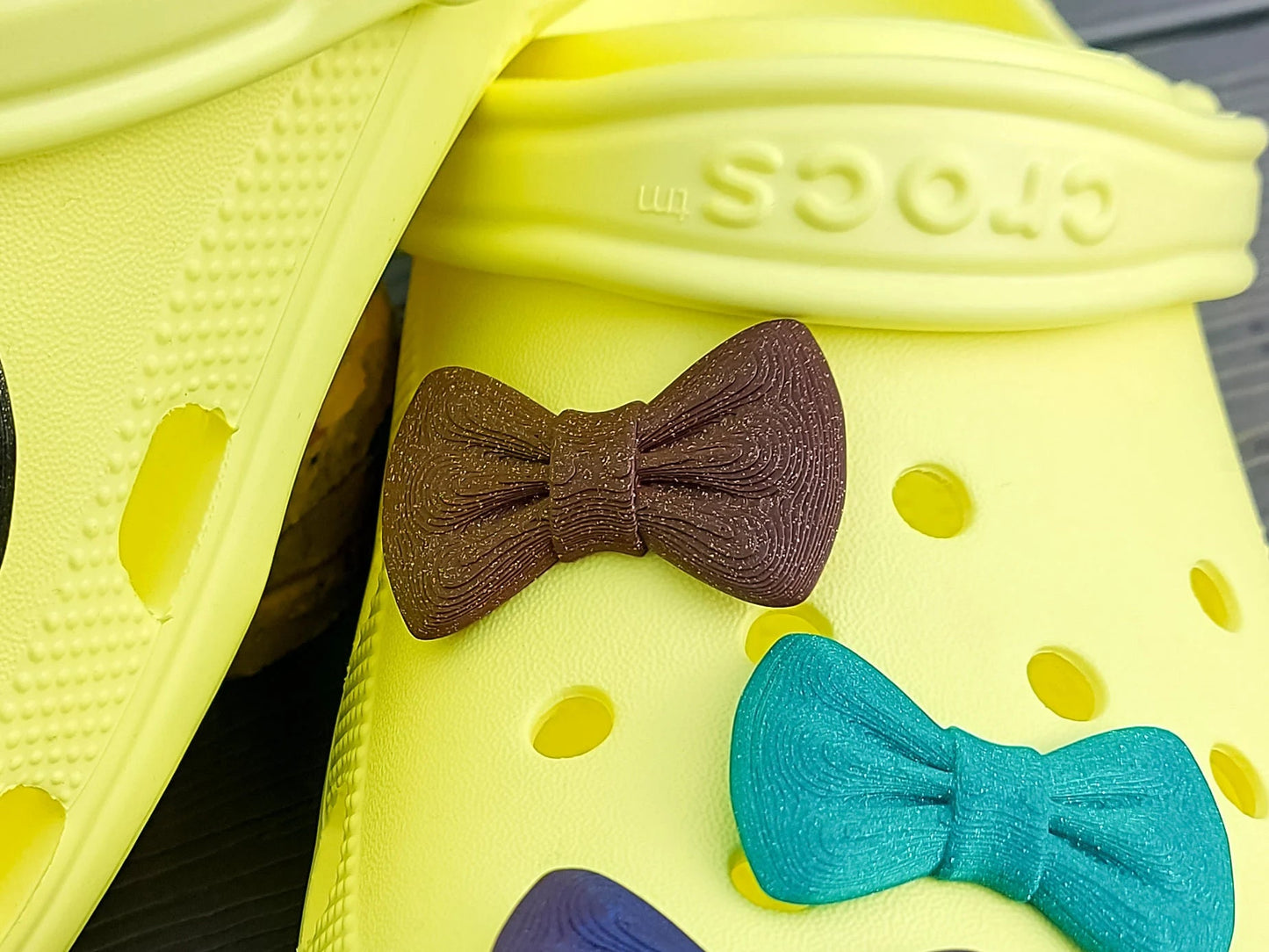 3d-printed bow shoe charms on a pair of shoes shoes. Multiple colors and they have a sparkly glitter.