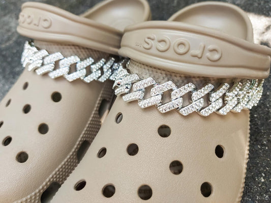 Rhinestone Cuban link shoe chain attached to a pair of shoes, showcasing the luxurious and sparkling design. The chain glimmers with rhinestones, adding a high-end, glamorous touch to the shoes, perfect for those who love to accessorize with bling