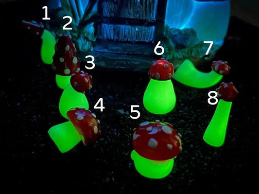 Glow in the dark forest mushroom shoe charms with white stems and red caps with white dots on a pair of shoes shoes.
