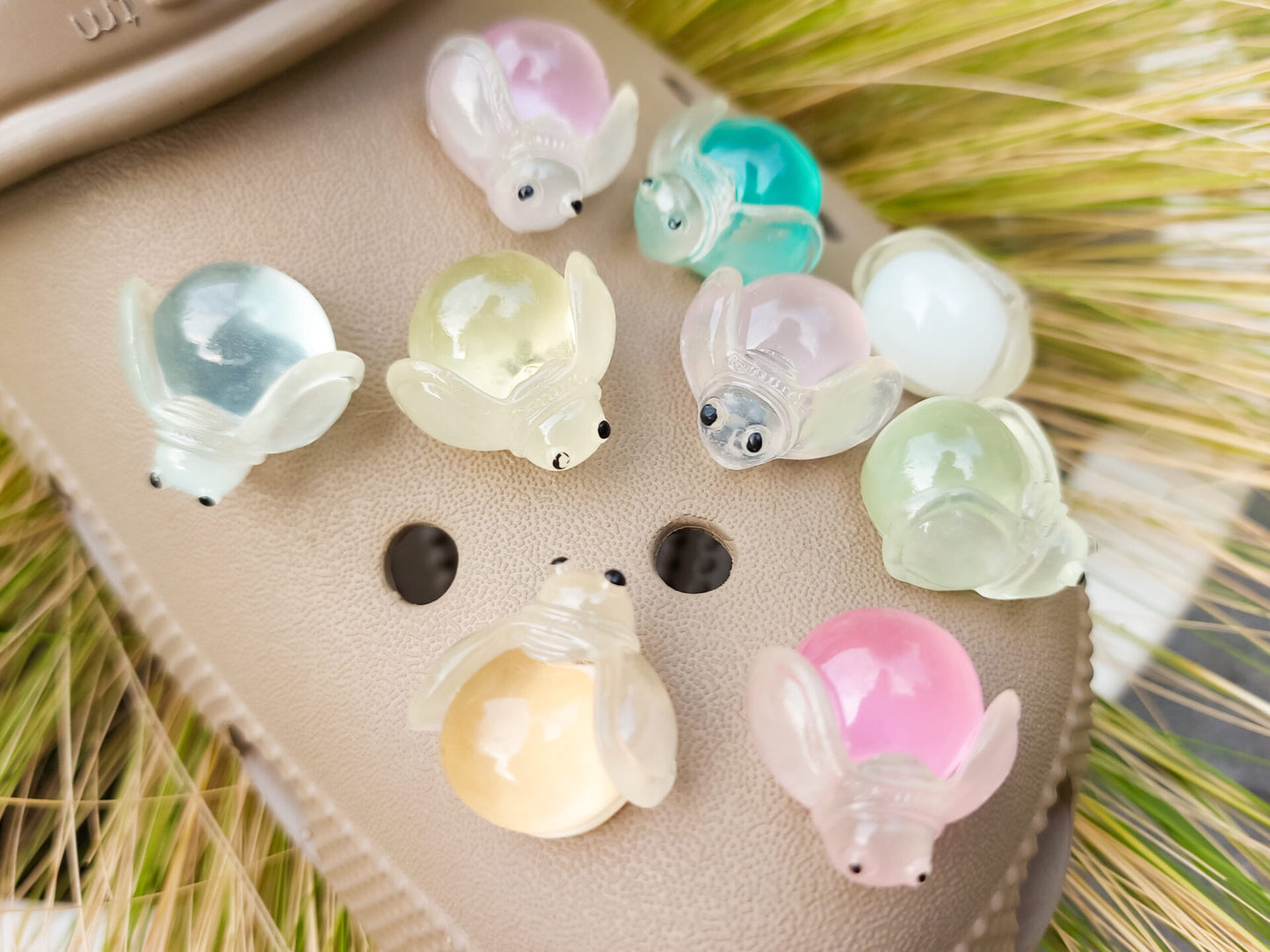 Close-up of glow-in-the-dark firefly charms on beige shoes, surrounded by vibrant pink flowers. The charming fireflies light up in different colors, creating a magical and whimsical look, perfect for adding a soft, glowing touch to your footwear.