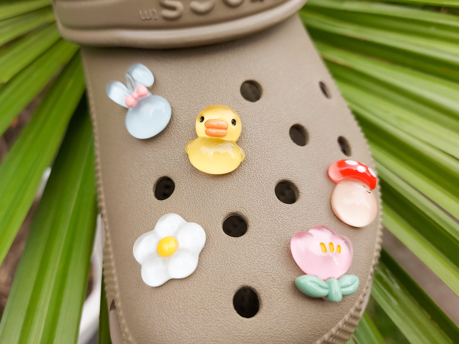 Close-up of a shoe decorated with a 5-piece jelly charm set, including two flowers, a yellow duck, a bunny with a pink bow, and a red mushroom. Each charm has a cute, soft, jelly-like appearance, adding a fun and playful vibe to the footwear.