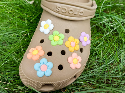 A cluster of vibrant cosmos flower charms decorates a clog shoe, with each charm showcasing delicate petals in shades of pink, white, and purple. The intricate details of the flowers mimic real cosmos blooms, with soft gradients and textured centers
