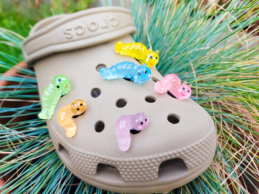 A collection of glow worm caterpillar shoe charms attached to a single shoe shoe. The charms feature caterpillar designs in various bright colors, including green, yellow, blue, pink, and orange, all designed to glow in the dark.