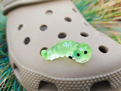 A collection of glow worm caterpillar shoe charms attached to a single shoe shoe. The charms feature caterpillar designs in various bright colors, including green, yellow, blue, pink, and orange, all designed to glow in the dark.