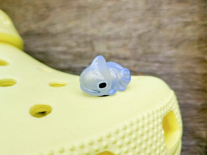 A close-up of a yellow shoe shoe with vibrant glow-in-the-dark chameleon charms in different colors (green, orange, pink, blue, and yellow) displayed outdoors on green grass.