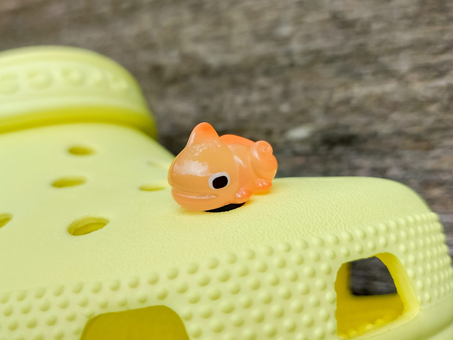 A close-up of a yellow shoe shoe with vibrant glow-in-the-dark chameleon charms in different colors (green, orange, pink, blue, and yellow) displayed outdoors on green grass.
