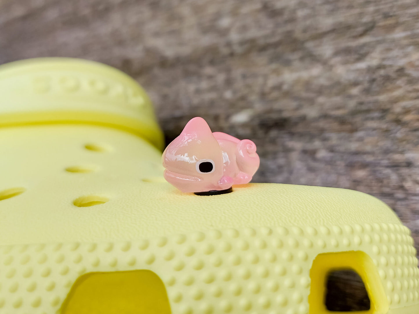 A close-up of a yellow shoe shoe with vibrant glow-in-the-dark chameleon charms in different colors (green, orange, pink, blue, and yellow) displayed outdoors on green grass.