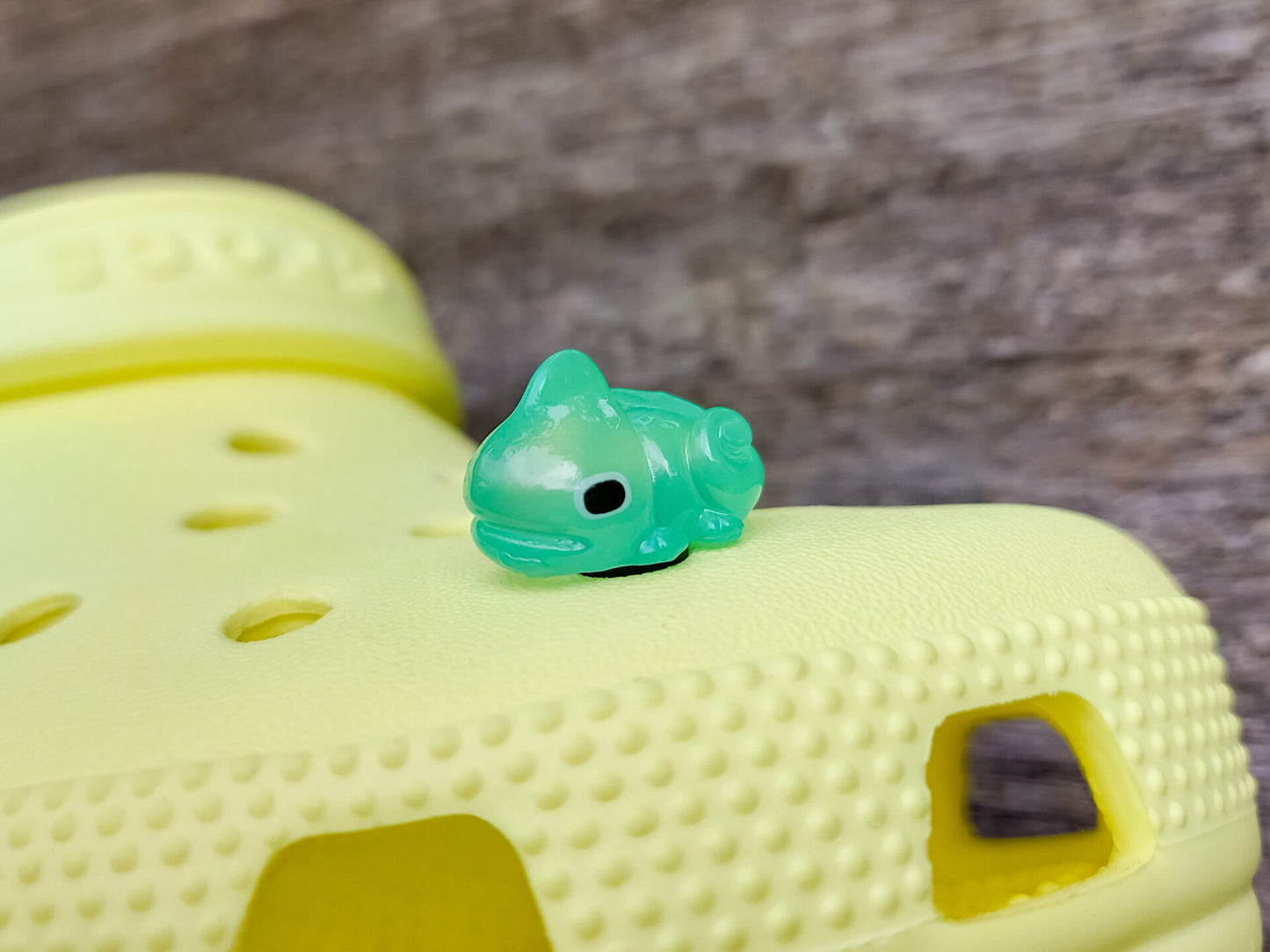 A close-up of a yellow shoe shoe with vibrant glow-in-the-dark chameleon charms in different colors (green, orange, pink, blue, and yellow) displayed outdoors on green grass.