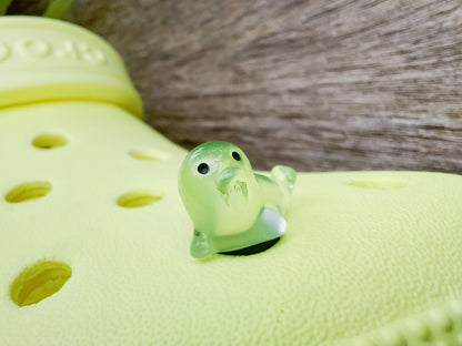 A yellow shoe shoe adorned with colorful glow-in-the-dark seal charms in shades of pink, blue, green, yellow, and purple, set against a natural background with blades of grass.