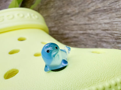 A yellow shoe shoe adorned with colorful glow-in-the-dark seal charms in shades of pink, blue, green, yellow, and purple, set against a natural background with blades of grass.