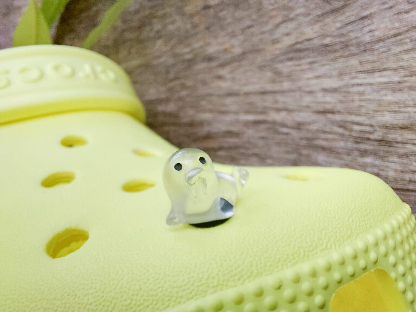 A yellow shoe shoe adorned with colorful glow-in-the-dark seal charms in shades of pink, blue, green, yellow, and purple, set against a natural background with blades of grass.