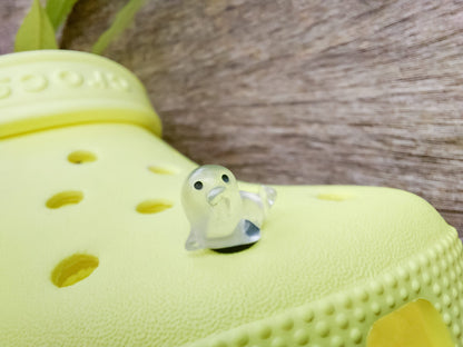 A yellow shoe shoe adorned with colorful glow-in-the-dark seal charms in shades of pink, blue, green, yellow, and purple, set against a natural background with blades of grass.