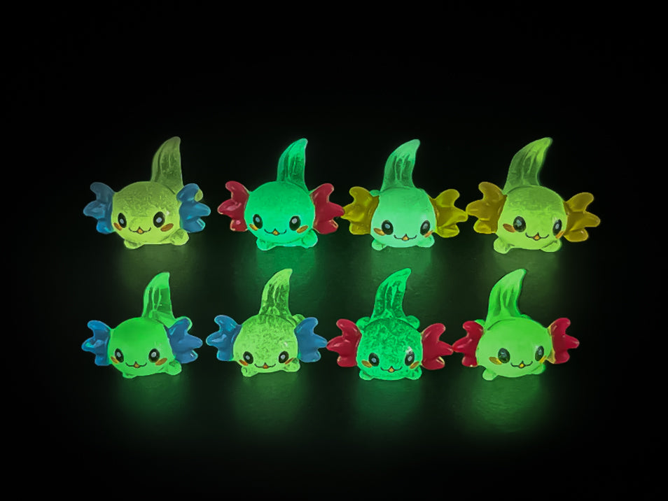 A yellow shoe shoe featuring colorful glow-in-the-dark axolotl charms in shades of green, pink, blue, orange, and silver, displayed outdoors on a wooden surface. The charms, with smiling faces and frilly gills, brighten the shoe.