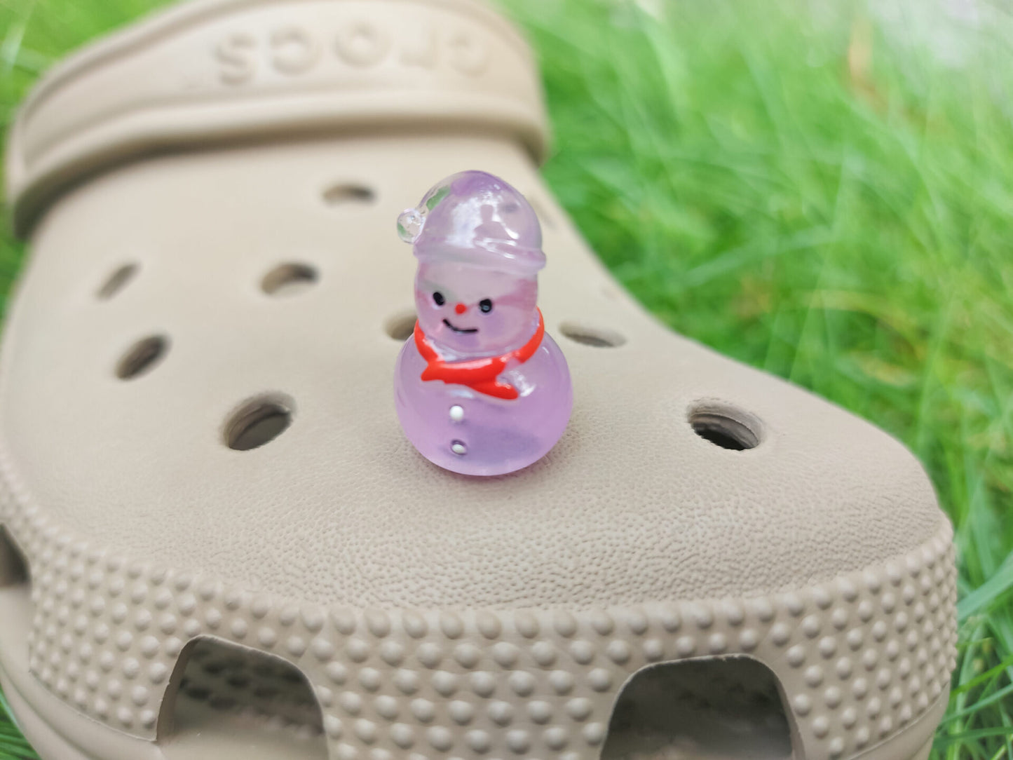 Glow-in-the-dark snowmen charms adorning a beige shoes shoe. The snowmen are in vibrant colors like green, yellow, red, purple, orange, and blue. Each snowman has a scarf, and a small hat, radiating a festive vibe perfect for the holiday season.