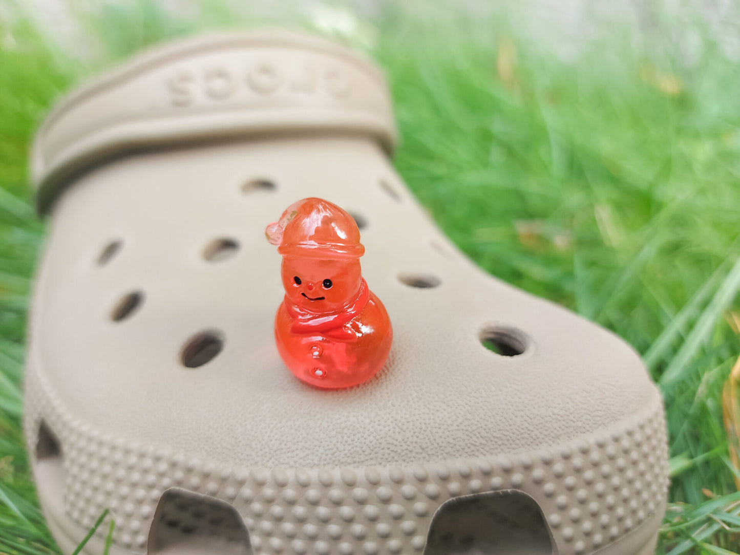 Glow-in-the-dark snowmen charms adorning a beige shoes shoe. The snowmen are in vibrant colors like green, yellow, red, purple, orange, and blue. Each snowman has a scarf, and a small hat, radiating a festive vibe perfect for the holiday season.