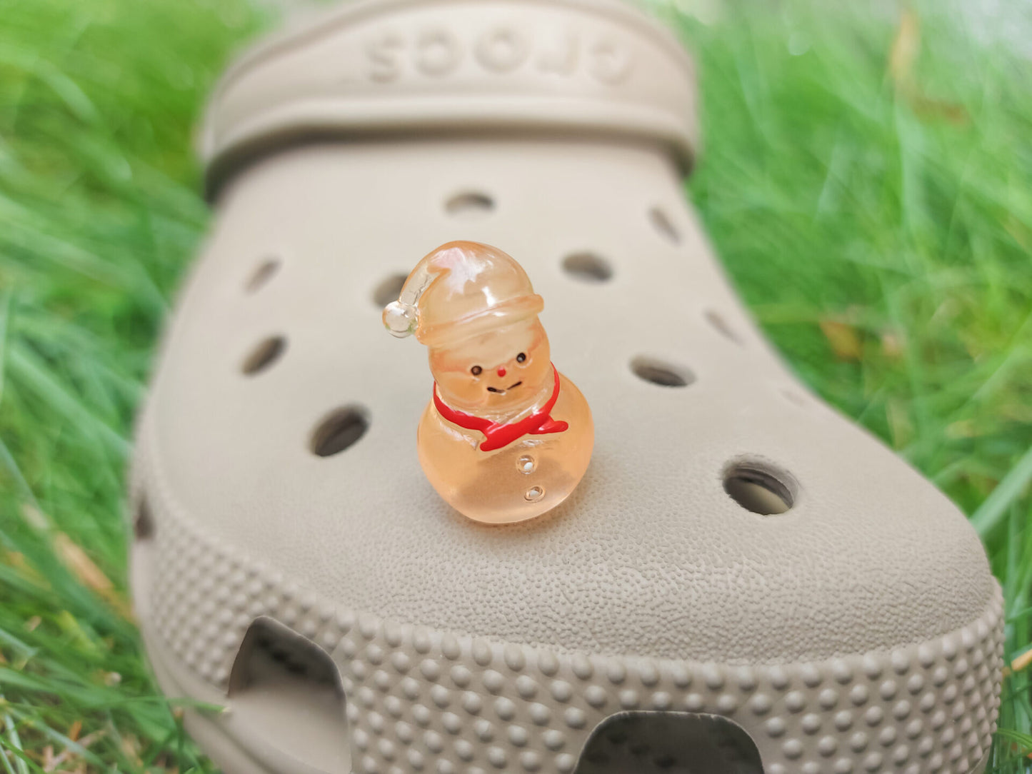 Glow-in-the-dark snowmen charms adorning a beige shoes shoe. The snowmen are in vibrant colors like green, yellow, red, purple, orange, and blue. Each snowman has a scarf, and a small hat, radiating a festive vibe perfect for the holiday season.