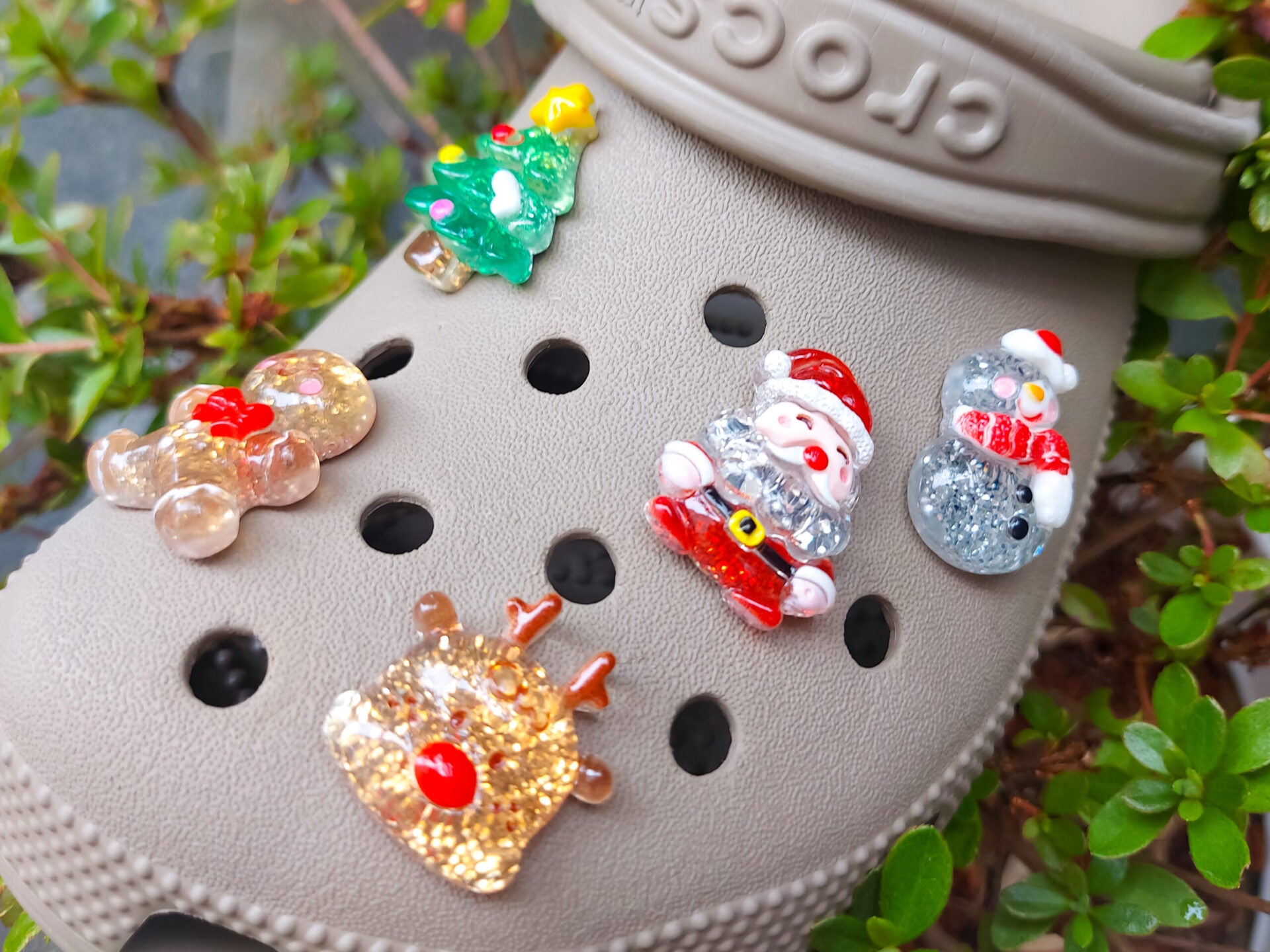 A glittery Christmas-themed set of five shoe charms featuring a gingerbread man, reindeer, snowman, Santa, and a Christmas tree. Each charm has a sparkling glitter finish, adding a festive and playful holiday touch to your shoes.