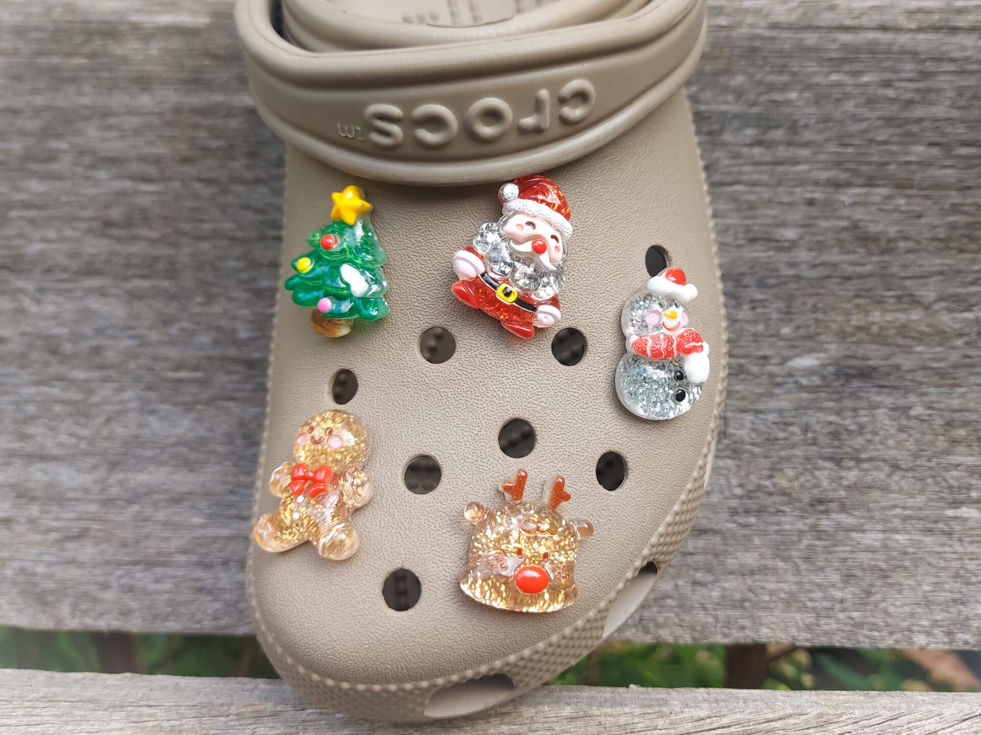 A glittery Christmas-themed set of five shoe charms featuring a gingerbread man, reindeer, snowman, Santa, and a Christmas tree. Each charm has a sparkling glitter finish, adding a festive and playful holiday touch to your shoes.