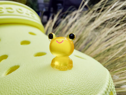Glow-in-the-dark frog charms on a yellow shoes shoe. These playful and luminous accessories add a fun, froggy touch to your footwear, making them perfect for customizing your shoes with a whimsical and adventurous vibe.