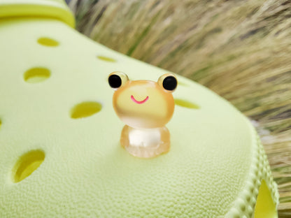 Glow-in-the-dark frog charms on a yellow shoes shoe. These playful and luminous accessories add a fun, froggy touch to your footwear, making them perfect for customizing your shoes with a whimsical and adventurous vibe.