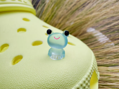 Glow-in-the-dark frog charms on a yellow shoes shoe. These playful and luminous accessories add a fun, froggy touch to your footwear, making them perfect for customizing your shoes with a whimsical and adventurous vibe.
