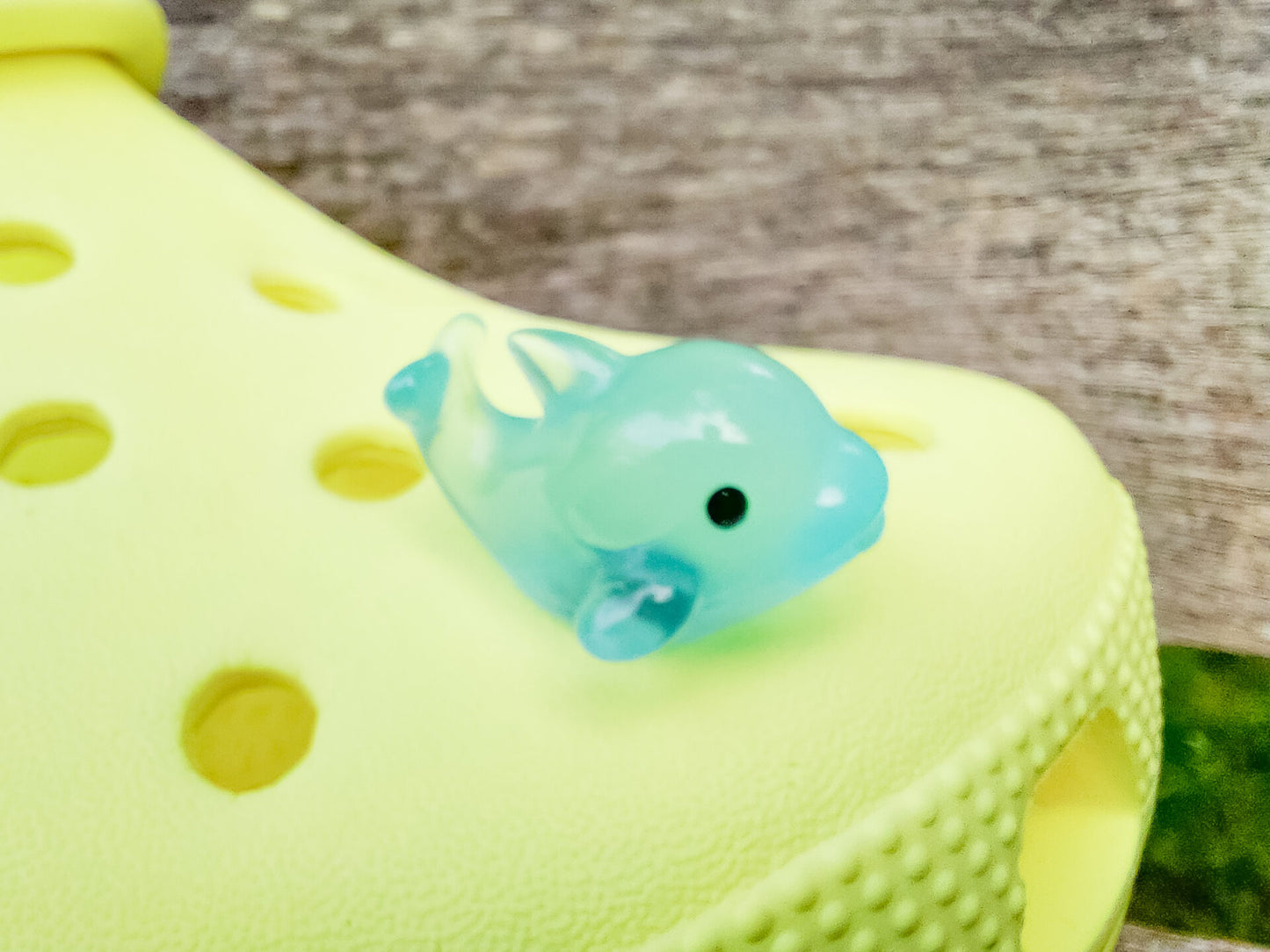 Six glow-in-the-dark dolphin charms in various pastel colors, including purple, pink, orange, green, blue, and white, are arranged on a yellow shoes shoe. The dolphins have tiny black eyes and wide grins, giving them a playful and cute appearance.