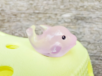 Six glow-in-the-dark dolphin charms in various pastel colors, including purple, pink, orange, green, blue, and white, are arranged on a yellow shoes shoe. The dolphins have tiny black eyes and wide grins, giving them a playful and cute appearance.