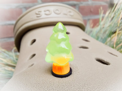 A beige shoes shoe adorned with small, glowing Christmas tree charms in a variety of soft colors, including yellow, pink, green, and blue. Each tree charm has a luminous effect, creating a festive and playful look.