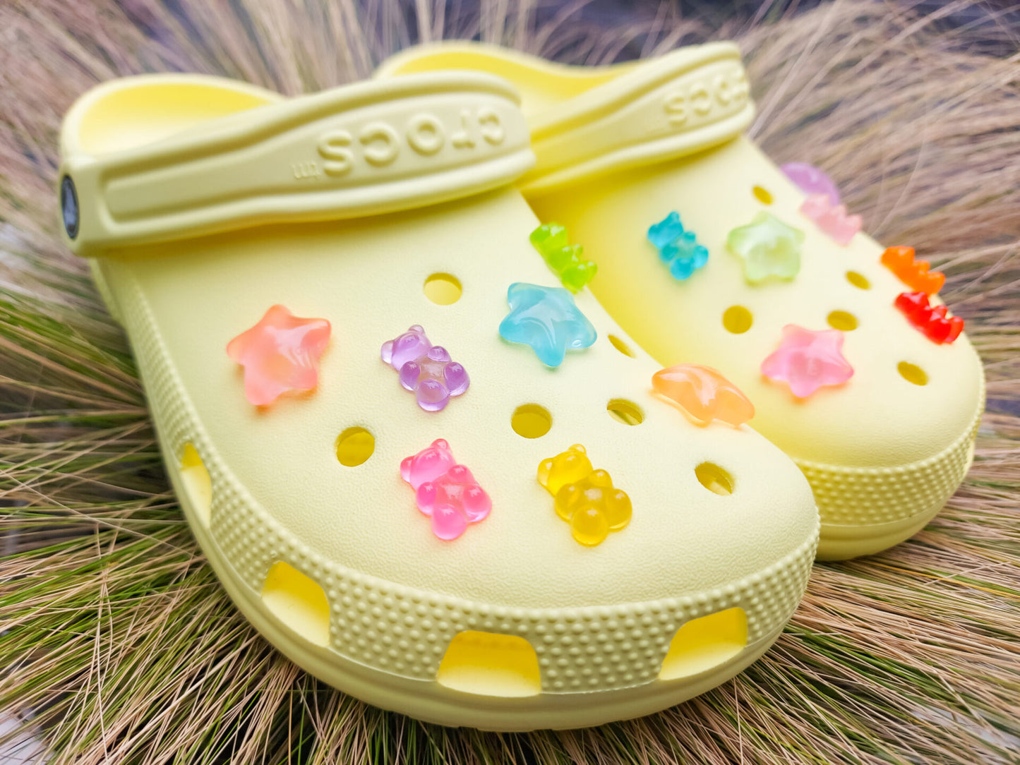 Close-up of yellow shoes featuring 14 colorful glow-in-the-dark gummy bear and star charms in shades of red, orange, pink, green, purple, and blue, arranged on the shoes, glowing softly in daylight against the bright background.