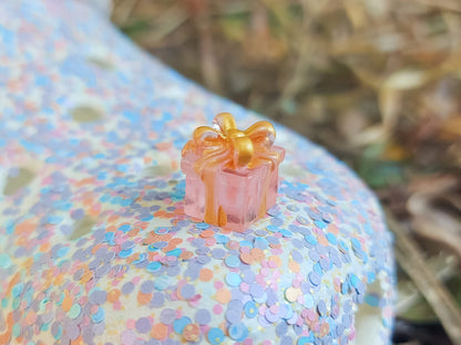 Glow in the dark christmas present charms on a colorful shoes shoe. It is a gift box with a big ribbon on top available in blue, pink, green, orange and peach. Xmas-themed perfect for the holidays.