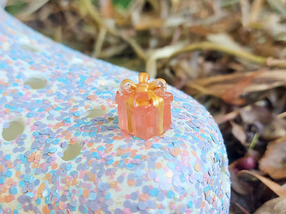 Glow in the dark christmas present charms on a colorful shoes shoe. It is a gift box with a big ribbon on top available in blue, pink, green, orange and peach. Xmas-themed perfect for the holidays.