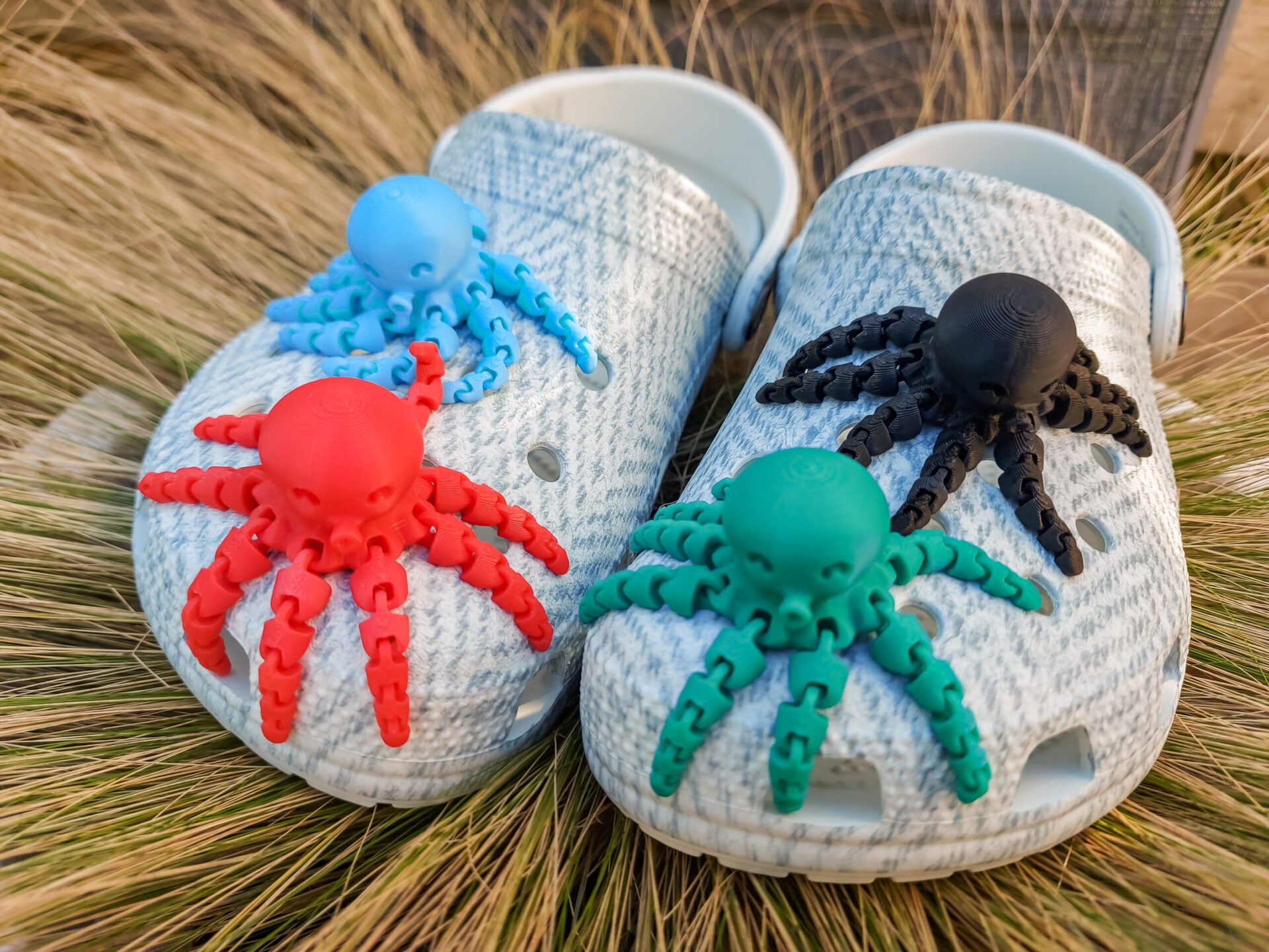 A set of colorful 3D printed flexi octopus charms in red, blue, green, and black, displayed on shoes shoes. Each charm features flexible, articulated tentacles, adding a fun ocean-themed touch and unique texture to the shoes.
