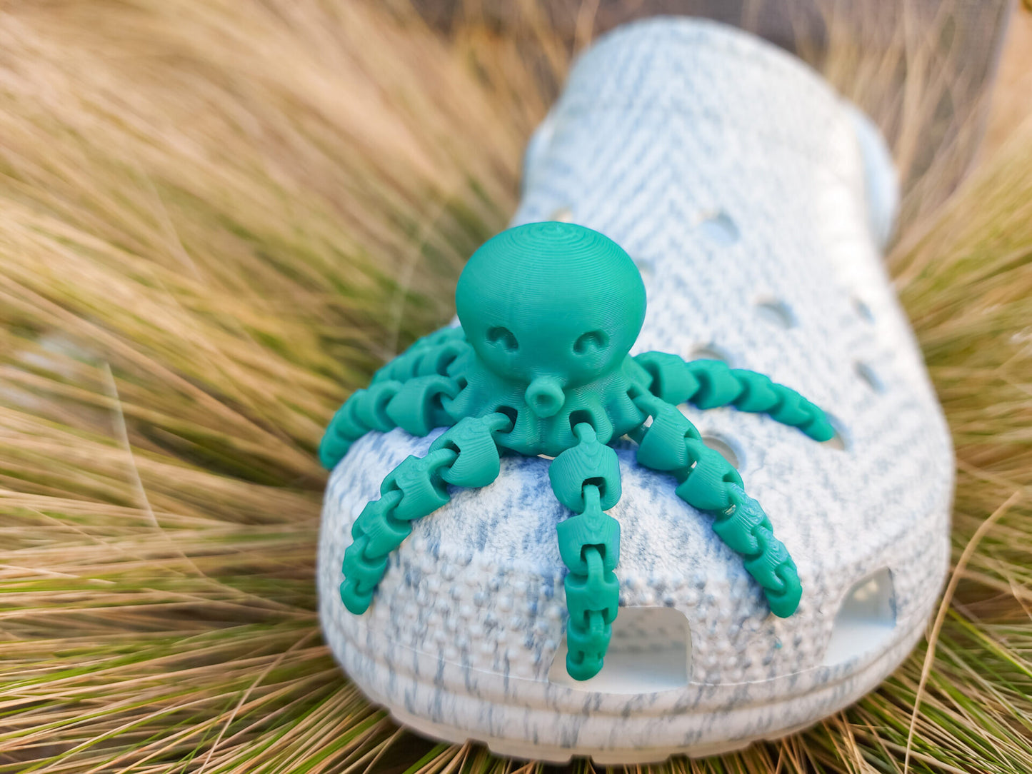 A set of colorful 3D printed flexi octopus charms in red, blue, green, and black, displayed on shoes shoes. Each charm features flexible, articulated tentacles, adding a fun ocean-themed touch and unique texture to the shoes.