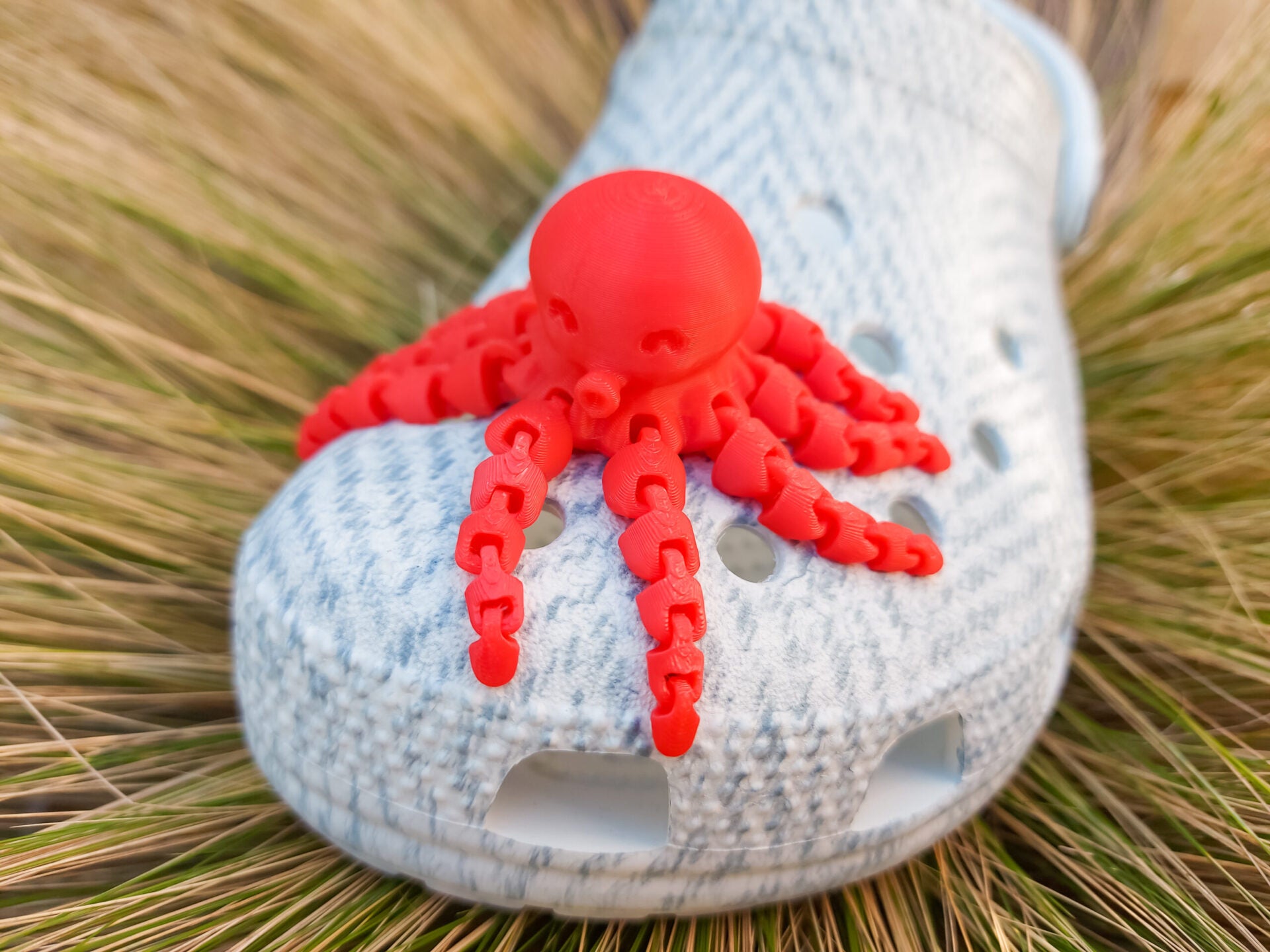 A set of colorful 3D printed flexi octopus charms in red, blue, green, and black, displayed on shoes shoes. Each charm features flexible, articulated tentacles, adding a fun ocean-themed touch and unique texture to the shoes.