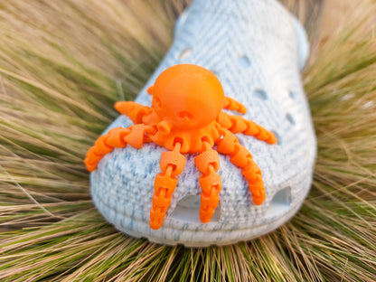 A set of colorful 3D printed flexi octopus charms in red, blue, green, and black, displayed on shoes shoes. Each charm features flexible, articulated tentacles, adding a fun ocean-themed touch and unique texture to the shoes.