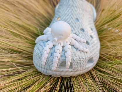 A set of colorful 3D printed flexi octopus charms in red, blue, green, and black, displayed on shoes shoes. Each charm features flexible, articulated tentacles, adding a fun ocean-themed touch and unique texture to the shoes.