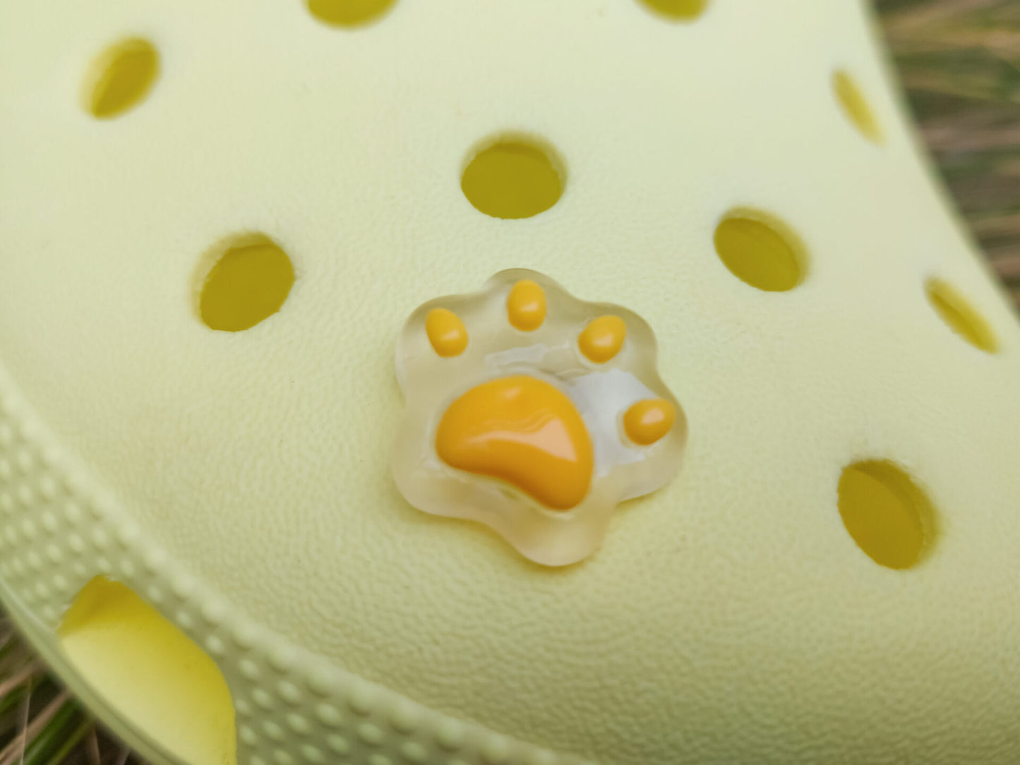 Glow-in-the-dark pastel paw print charms in pink, yellow, blue, and green, attached to a yellow shoe. The charms have a soft glow effect and add a playful animal-inspired look.