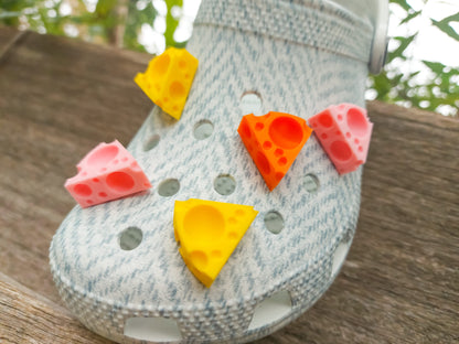 Close-up of a pair of light blue shoes decorated with colorful 3D-printed cheese wedge charms in shades of yellow, orange, and pink. The cheese charms feature realistic holes and a playful, quirky design, adding a fun pop of color to the footwear.
