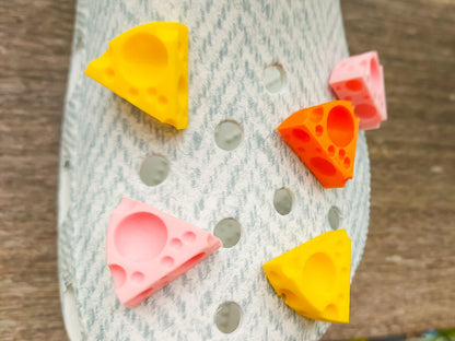 Close-up of a pair of light blue shoes decorated with colorful 3D-printed cheese wedge charms in shades of yellow, orange, and pink. The cheese charms feature realistic holes and a playful, quirky design, adding a fun pop of color to the footwear.