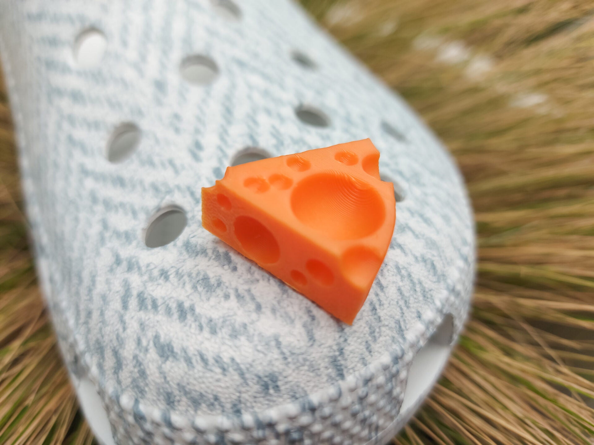Close-up of a pair of light blue shoes decorated with colorful 3D-printed cheese wedge charms in shades of yellow, orange, and pink. The cheese charms feature realistic holes and a playful, quirky design, adding a fun pop of color to the footwear.