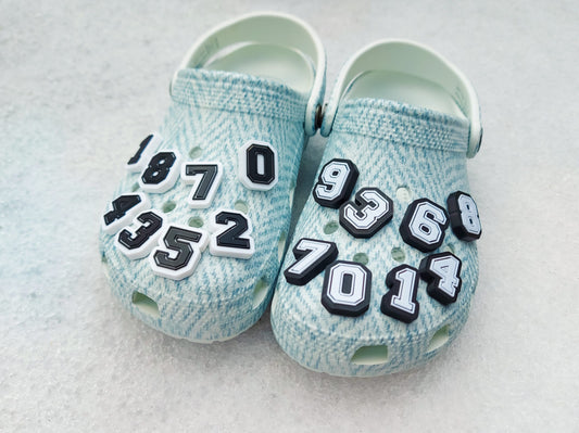 A pair of blue-patterned shoes featuring custom 3D-printed number charms, showcasing the digits 0 through 9 in sleek black and white colors. Each charm is securely clipped into the shoe holes, standing out with a bold varsity-inspired style.