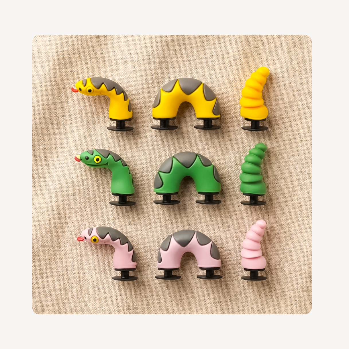 Three colorful snake-shaped clog charms arranged in a 3x3 grid on a textured beige square background, with a light gray outer border.
