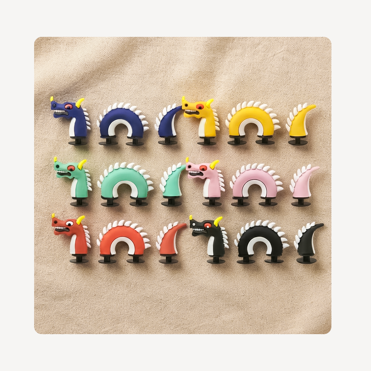 Six colorful dragon-shaped clog charms arranged in three rows on a beige textured background. The set includes blue, yellow, green, pink, red, black, and white versions, with some featuring small yellow horn accents.