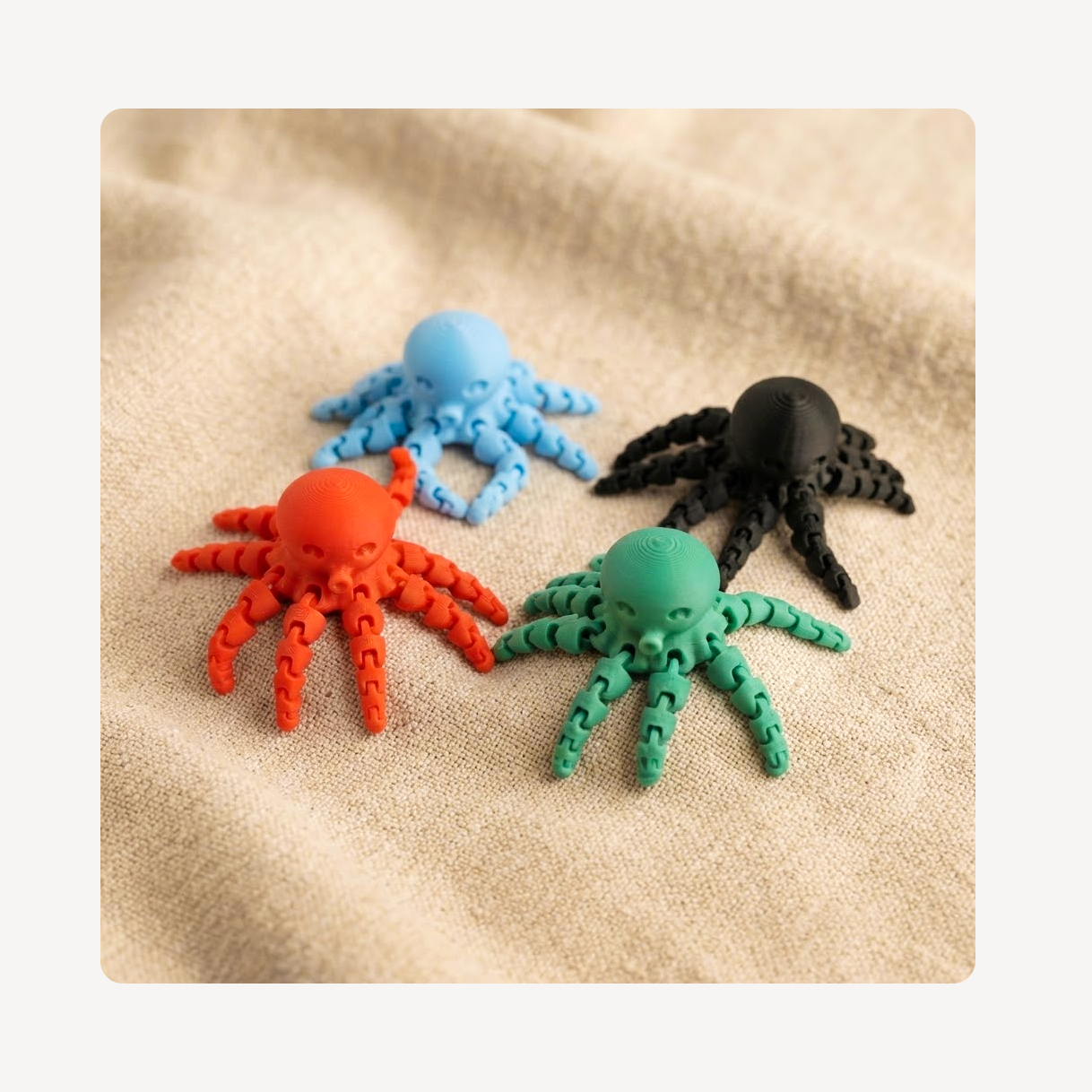 Four small octopus-shaped clog charms in red, light blue, green, and black, arranged on a beige textured fabric background.