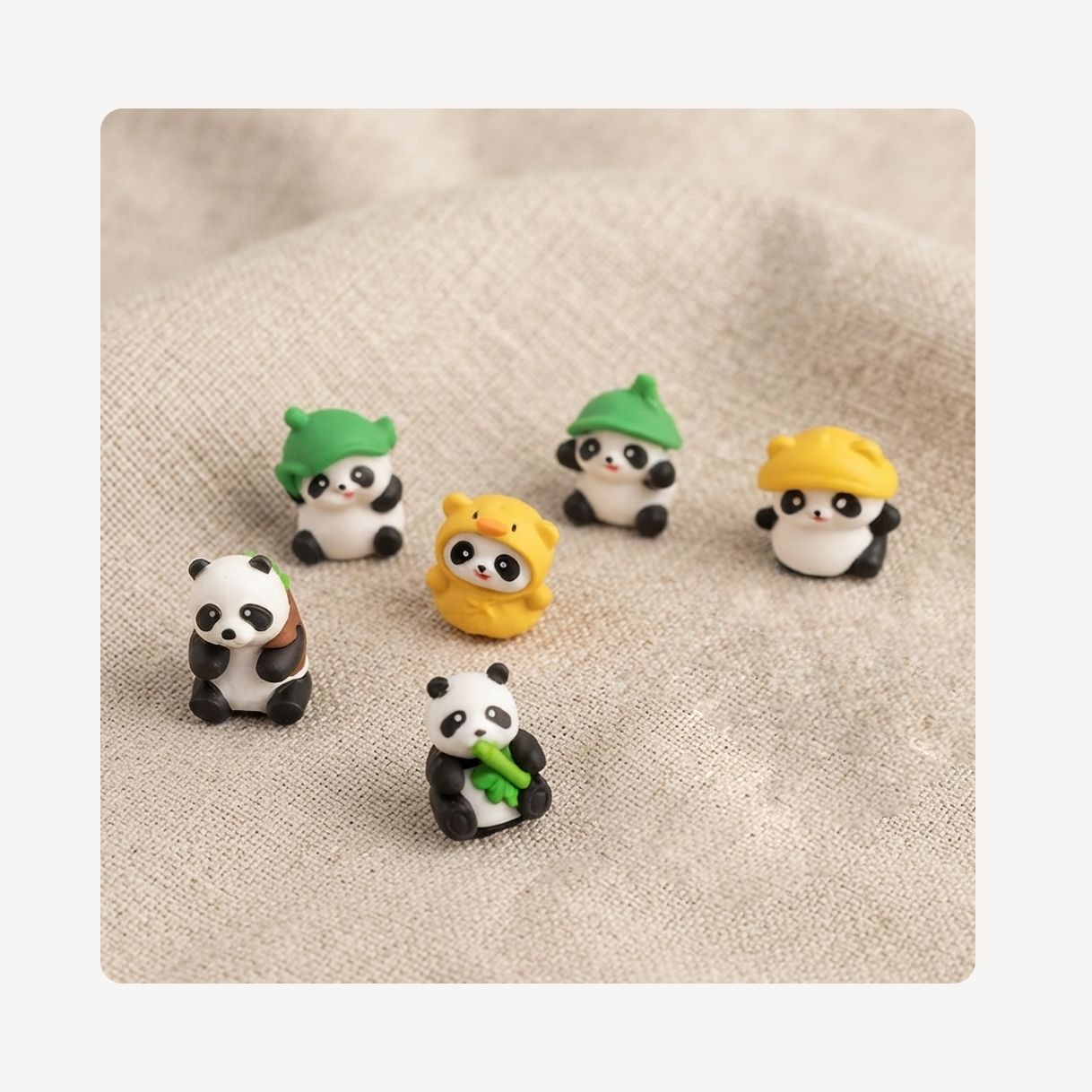 Five small panda-themed clog charms arranged on a beige textured fabric background. Three wear green hats, two wear yellow hats, and two are black-and-white pandas, one holding green bamboo.