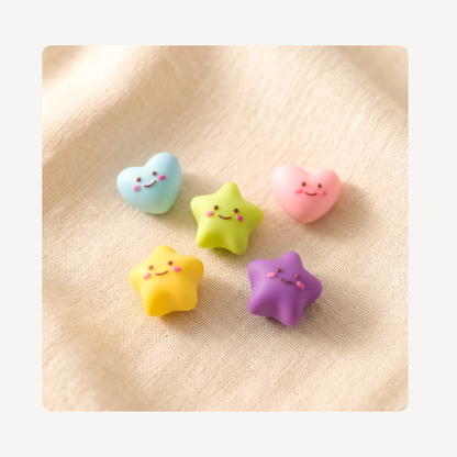 Five cute, small clog charms shaped like a heart and star in pastel colors, featuring simple smiling faces, arranged on a textured beige fabric background.